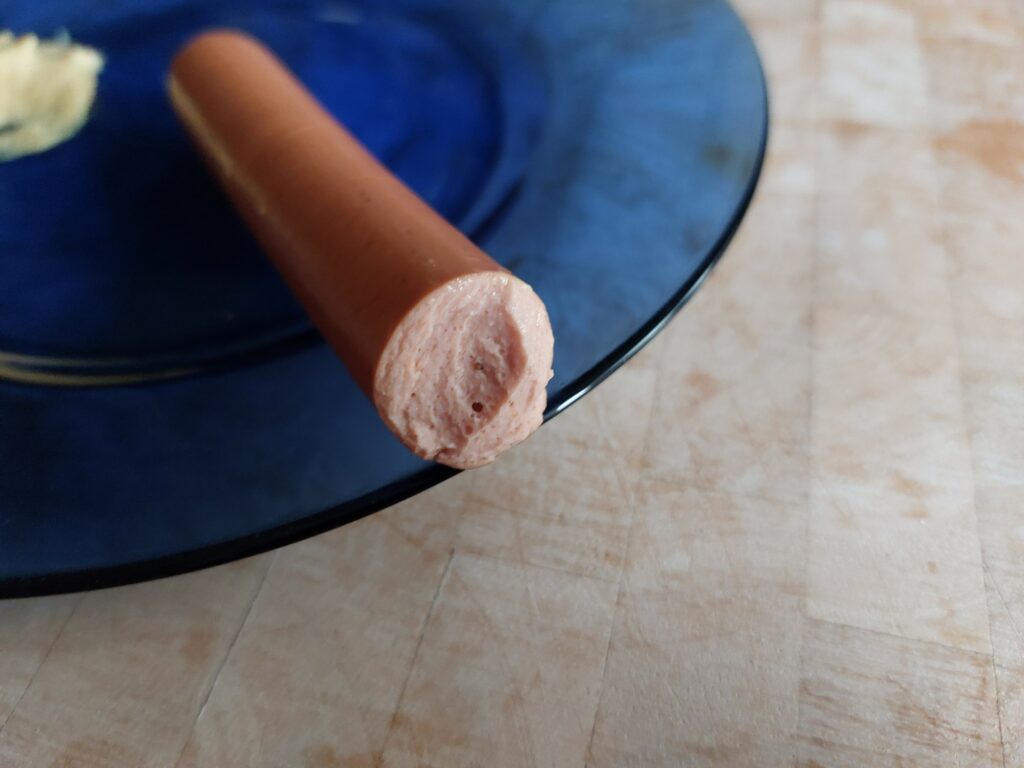 Angebissene vegetarische Wiener auf blauem Teller mit Senf