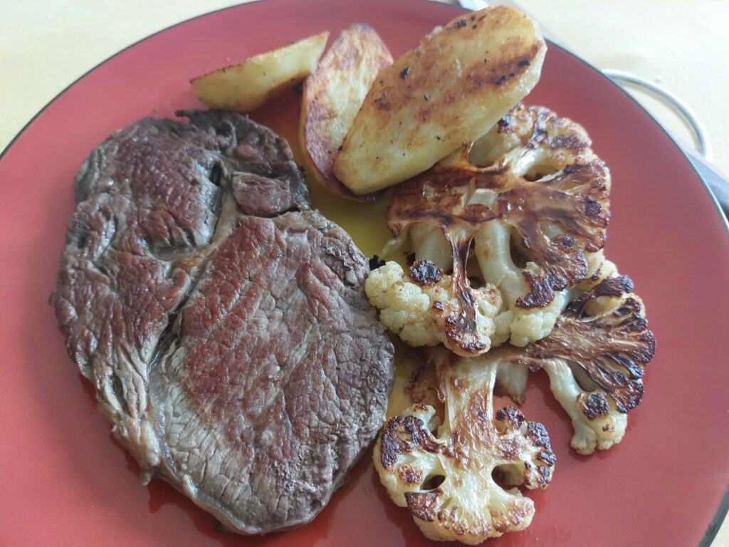 Grillplatte auf dem Teller (Rib-Eye-Steak, Blumenkohl, Kartoffel)